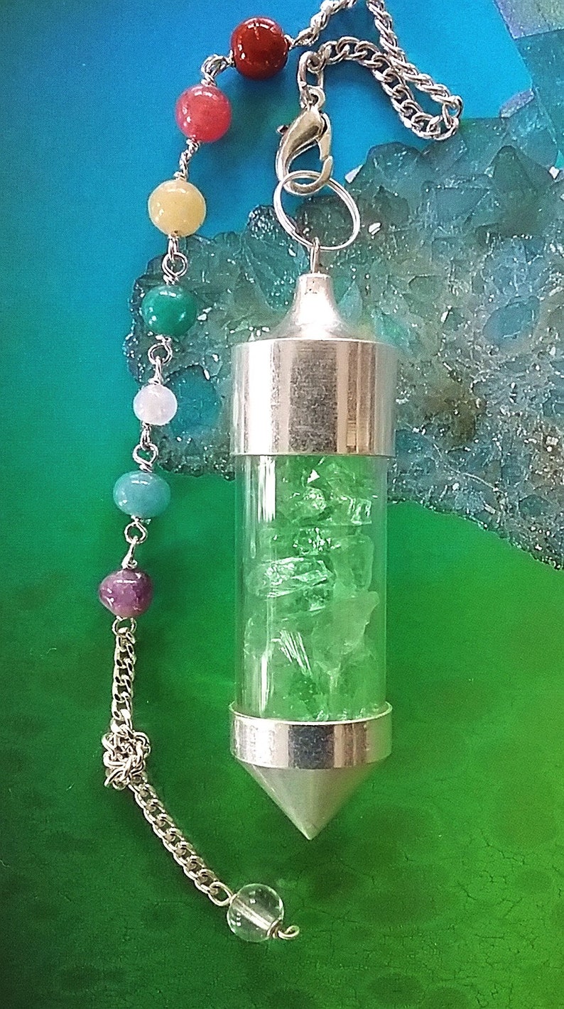 May include: A silver pendulum with a clear glass vial filled with green crystals. The pendulum is attached to a silver chain with a clear crystal at the end and a series of colorful beads.