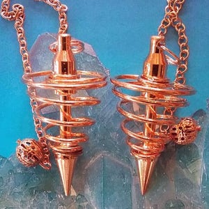 May include: Two copper spiral pendulums with chains and a ball at the end. The pendulums are on a blue and green background.