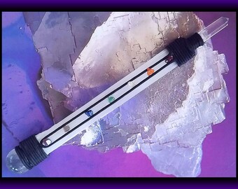 May include: A white crystal wand with a clear quartz tip and a black cord wrapped around the base. The wand has seven small, colorful stones embedded in the cord, representing the seven chakras.