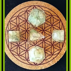 May include: Five clear green geometric crystal shapes on a brown cork coaster with a flower of life pattern. The crystals are a pyramid, a cube, and three dodecahedrons.