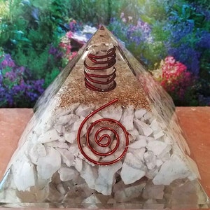 May include: A clear resin pyramid containing a layer of white stone fragments at the base, a layer of copper-colored metallic shavings in the middle, and a red wire coil wrapped around a clear crystal point near the top, with a red spiral wire on the front.