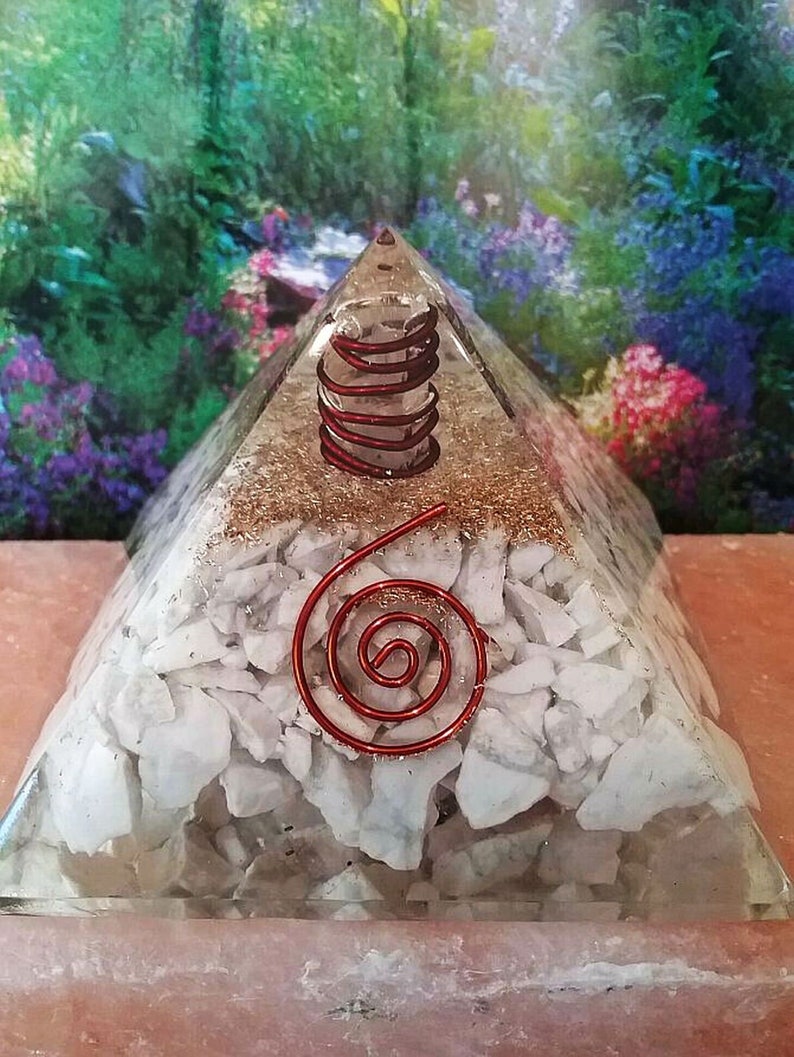 May include: A clear resin pyramid containing a layer of white stone fragments at the base, a layer of copper-colored metallic shavings in the middle, and a red wire coil wrapped around a clear crystal point near the top, with a red spiral wire on the front.