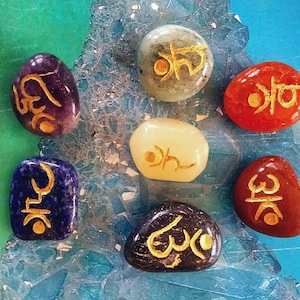 May include: Seven smooth, rounded stones with gold lettering on each. The stones are in various colours, including purple, green, white, red, blue, and black.
