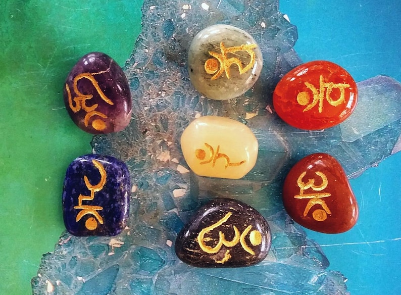 May include: Seven smooth, rounded stones with gold lettering on each. The stones are in various colours, including purple, green, white, red, blue, and black.