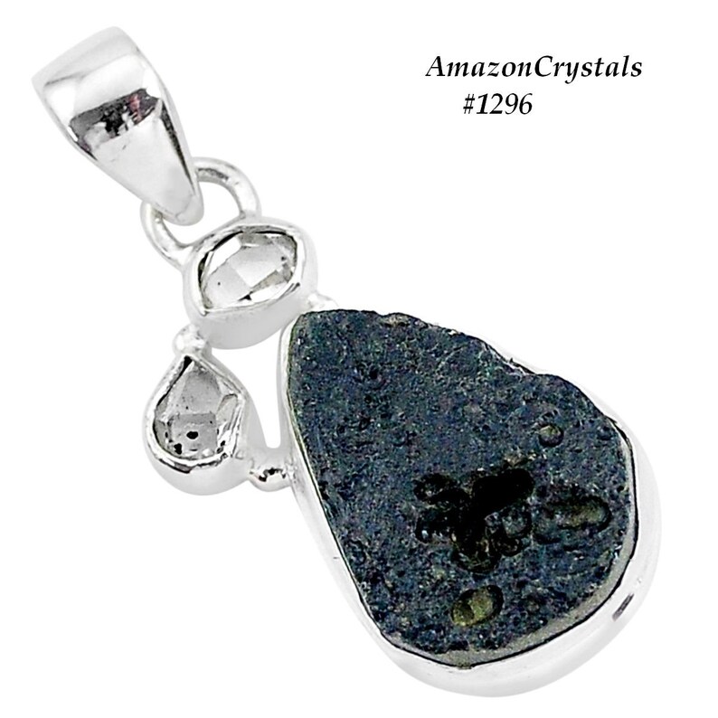 Pode incluir: Um pingente de prata com uma pedra preta em forma de l&aacute;grima e detalhes brancos. A pedra tem uma textura &aacute;spera e natural e est&aacute; engastada em uma moldura de prata. O pingente &eacute; acentuado por tr&ecirc;s pequenas pedras transparentes.