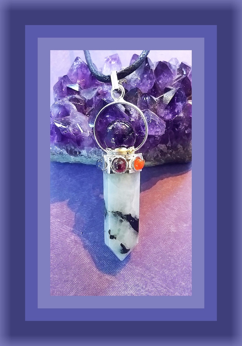 May include: A silver pendant with a clear crystal point, surrounded by a silver ring with a purple amethyst stone. The pendant is accented with red and orange stones and hangs from a black cord.