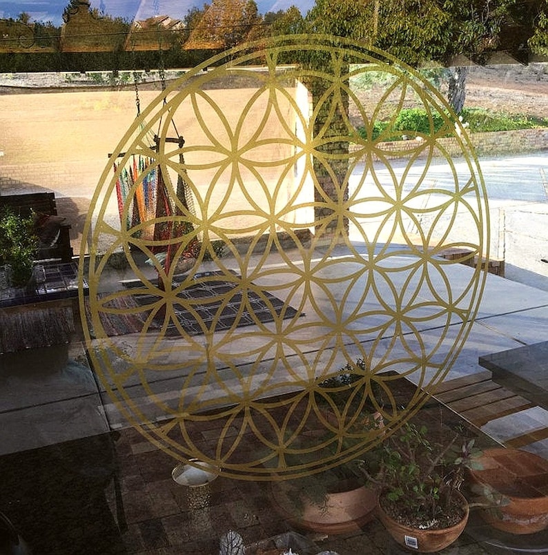 May include: A gold geometric pattern, known as the Flower of Life, is displayed on a glass window. The pattern is a repeating design of overlapping circles and is a popular symbol in spiritual and metaphysical practices.