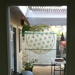 May include: A yellow flower of life mandala sticker on a glass door, with a view of a patio with a white pergola, a white shed, and a small table and chairs.