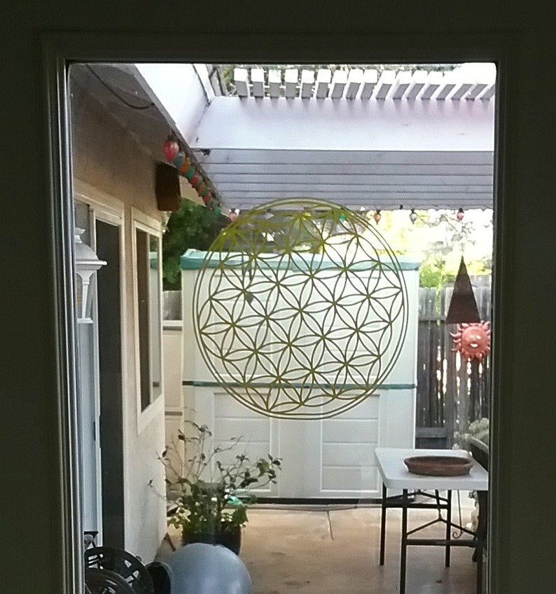 May include: A yellow flower of life mandala sticker on a glass door, with a view of a patio with a white pergola, a white shed, and a small table and chairs.