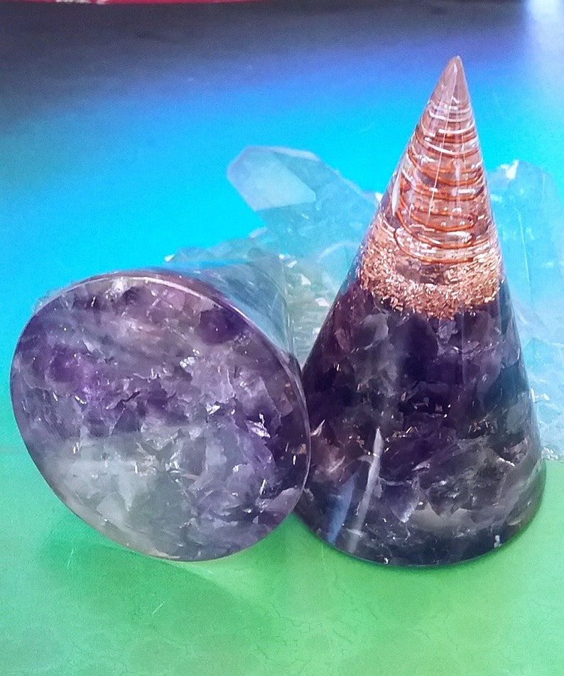 May include: Two amethyst crystal healing orgone pyramids, one is a cone shape with copper wire wrapped around it, the other is a flat disc shape.