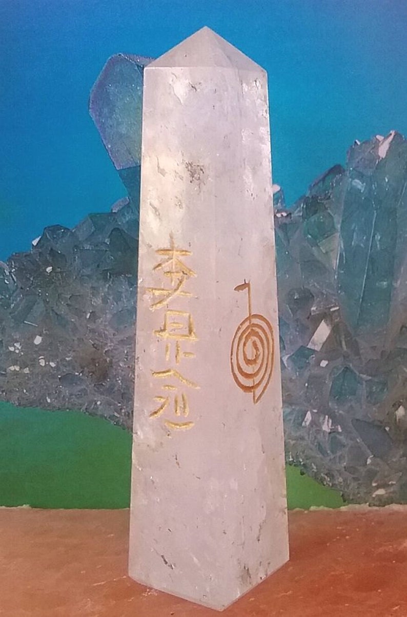 May include: A white crystal point with a gold inscription of the word "serenity" and a spiral symbol. The crystal is sitting on a brown surface.