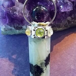 May include: A silver pendant with a clear crystal point, surrounded by a silver ring with a purple amethyst sphere inside. The pendant is accented with three smaller stones: two yellow and one green.