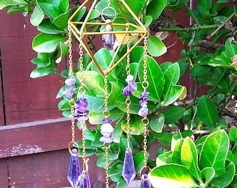 May include: A gold-coloured geometric wind chime with hanging chains and purple crystal accents. The wind chime features a diamond-shaped frame with smaller crystals and amethyst stones. The chains are suspended from a ring at the top, and the crystals are teardrop-shaped.