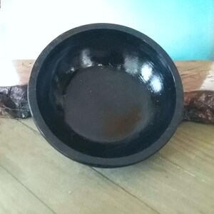 May include: A black wooden bowl with a smooth, glossy finish. The bowl is round and has a wide, shallow opening.