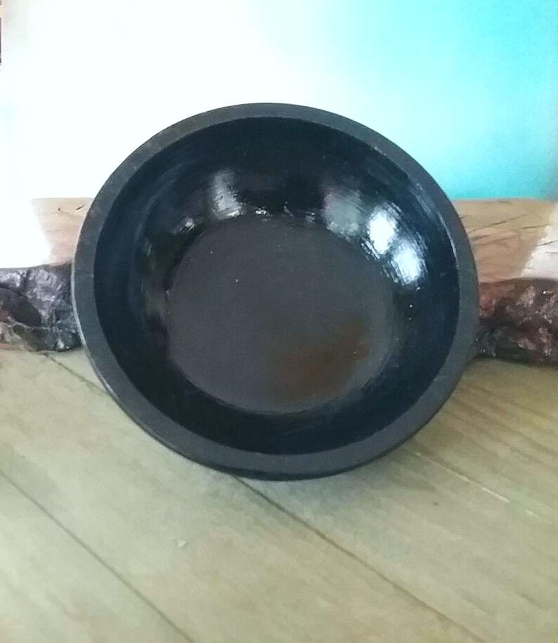 May include: A black wooden bowl with a smooth, glossy finish. The bowl is round and has a wide, shallow opening.
