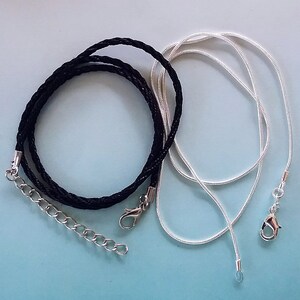 May include: Two necklaces, one black braided cord with a silver clasp and one silver chain.