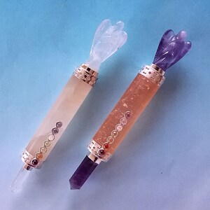 May include: Two crystal wands with angel-shaped tops. One is light orange with a clear crystal tip and a series of small, colourful stones. The other is a darker orange with a purple crystal tip and a series of small, colourful stones.
