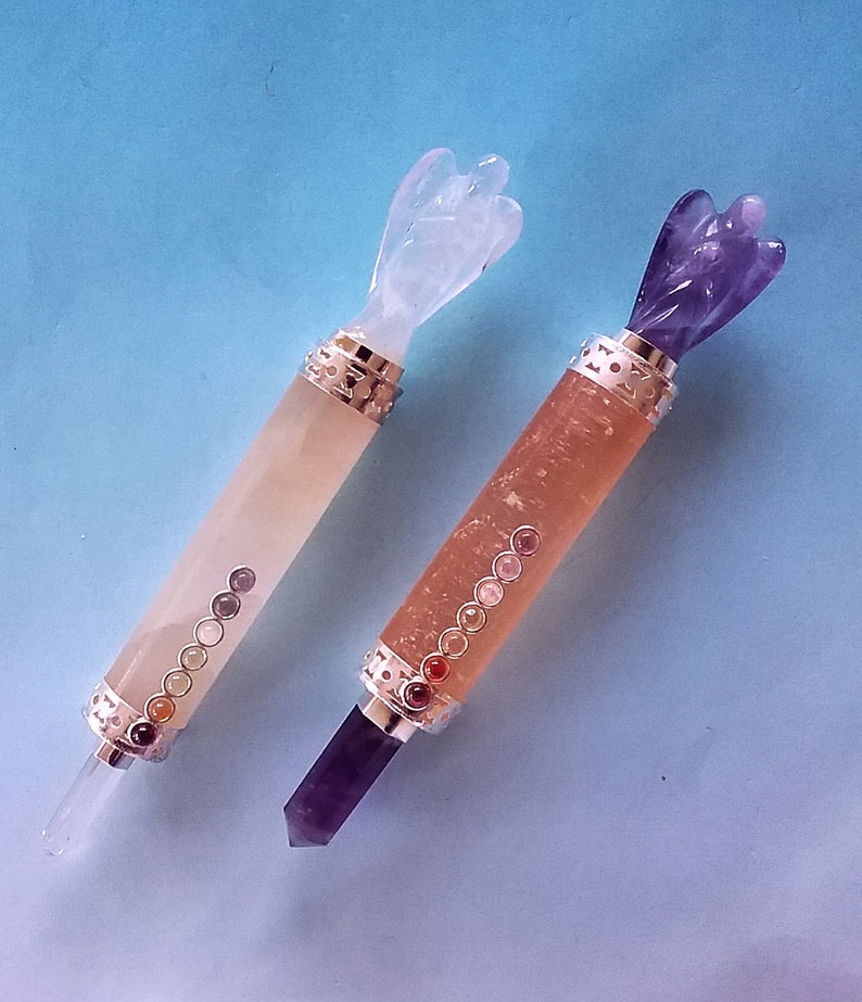 May include: Two crystal wands with angel-shaped tops. One is light orange with a clear crystal tip and a series of small, colourful stones. The other is a darker orange with a purple crystal tip and a series of small, colourful stones.