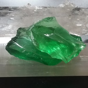 May include: A large, green, translucent crystal on a white, textured surface.