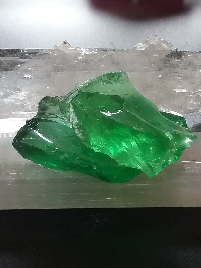 May include: A large, green, translucent crystal on a white, textured surface.