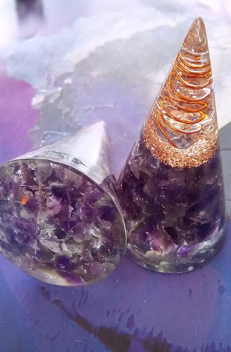 May include: Two amethyst crystal point orgonite pyramids with copper wire spirals. The pyramids are clear and filled with amethyst crystals. The copper wire spirals are visible through the clear resin.