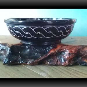 May include: A black slate bowl with a carved white design. The bowl is sitting on a piece of wood.