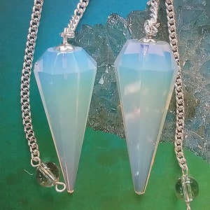 May include: Two white opal crystal pendulums with silver chains and green crystal beads. The pendulums are faceted and have a pointed tip.