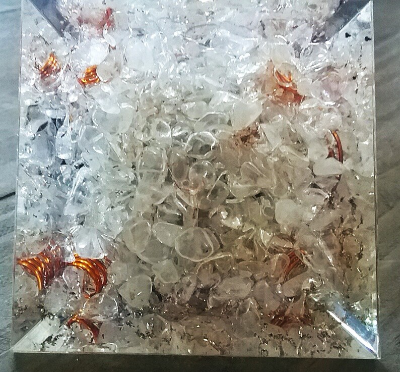 May include: A clear glass cube filled with small, clear quartz crystals and copper wire coils. The crystals are tightly packed together, and the copper wire coils are visible throughout the cube.