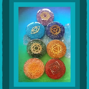 May include: Seven chakra stones, each with a different color and symbol. The stones are arranged in a pyramid shape, with the purple stone at the top and the red stone at the bottom.