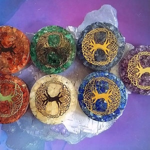 May include: Seven round, flat, crystal tree of life coasters. Each coaster is made of different coloured crystals, including red, orange, yellow, green, blue, purple, and clear. The tree of life design is gold and is centred on each coaster.