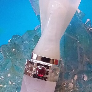 May include: White angel shaped crystal wand with a silver band and a red gemstone. The wand is sitting on a bed of blue crystals.