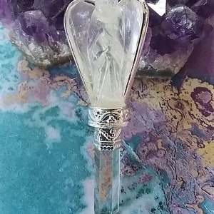 Op de afbeelding: Een heldere kristallen engelhanger met een zilveren ketting en een sierlijke zilveren rand. De hanger is gevormd als een engel met vleugels en een lange, puntige kristal aan de onderkant.