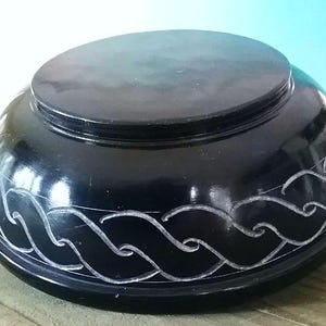 May include: A black, round, carved stone bowl with a wave design. The bowl is made of polished black stone and has a smooth, glossy finish.
