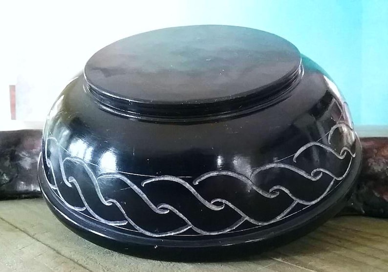 May include: A black, round, carved stone bowl with a wave design. The bowl is made of polished black stone and has a smooth, glossy finish.