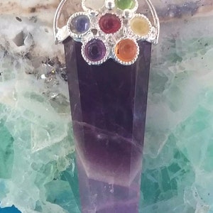 May include: A silver pendant with a purple amethyst point and a silver flower design with seven colorful gemstones. The gemstones are red, orange, yellow, green, blue, indigo, and violet.