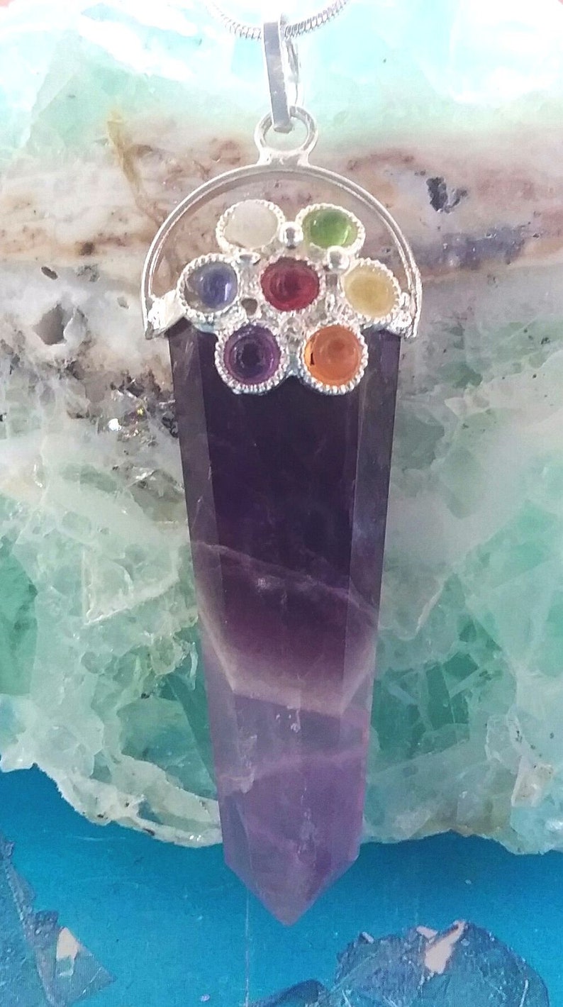 May include: A silver pendant with a purple amethyst point and a silver flower design with seven colorful gemstones. The gemstones are red, orange, yellow, green, blue, indigo, and violet.