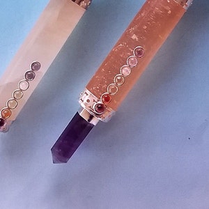 May include: Two crystal wands with silver detailing and coloured stones. One wand is pale pink with a clear crystal tip, the other is a darker pink with a purple crystal tip. The wands have a series of small, coloured stones.
