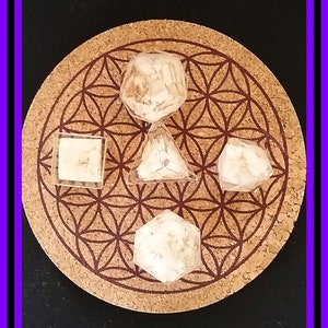 May include: Five clear crystal geometric shapes on a brown cork coaster with a flower of life pattern. The shapes are a cube, a pyramid, a rhombus, a hexagon, and a dodecahedron.