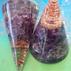 May include: Two amethyst crystal orgonite pyramids with copper wire spirals inside. The pyramids are clear and have a purple hue. The copper wire spirals are visible through the clear crystal.