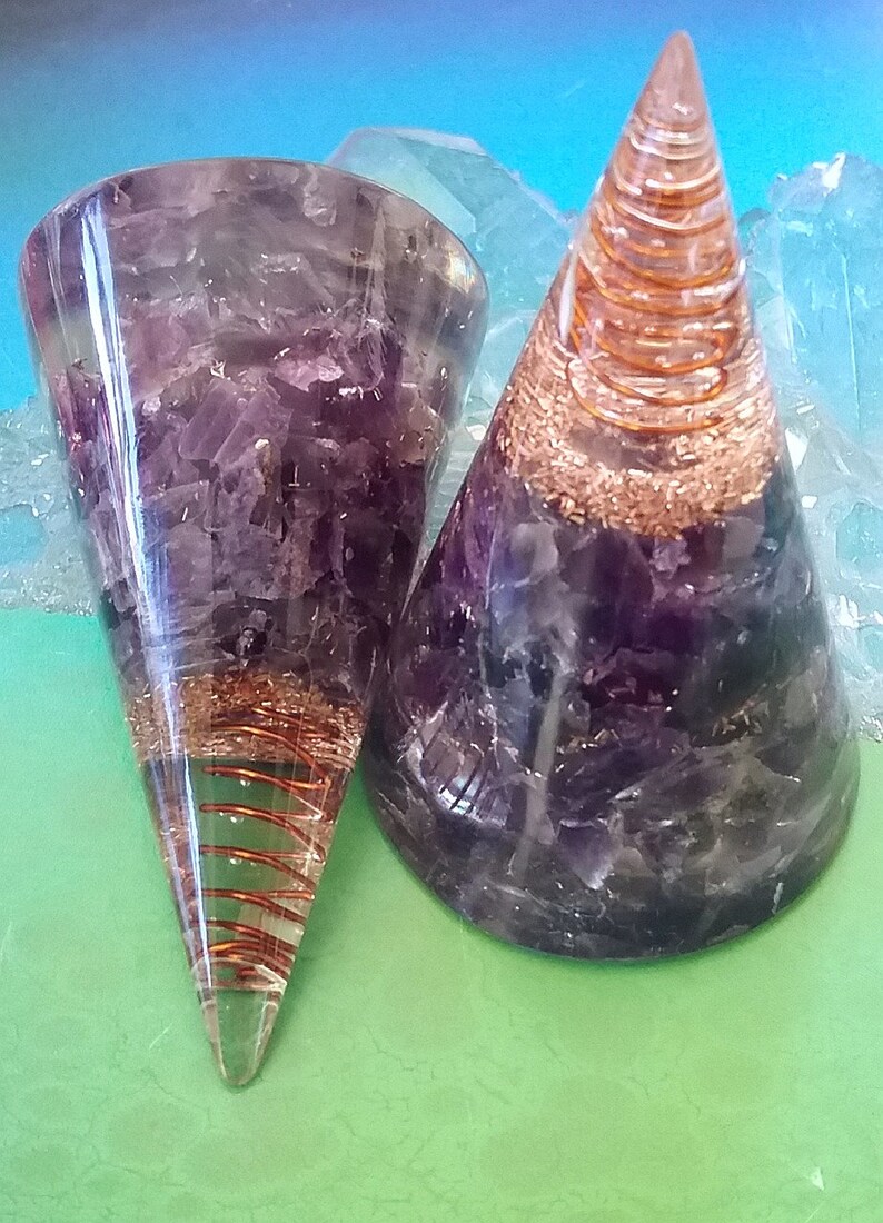May include: Two amethyst crystal orgonite pyramids with copper wire spirals inside. The pyramids are clear and have a purple hue. The copper wire spirals are visible through the clear crystal.