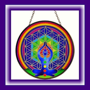 Op de afbeelding: Een kleurrijk glas-in-loodraam dat hangt met een regenboogmandala-ontwerp en een figuur in een yogapose met zeven chakra's.