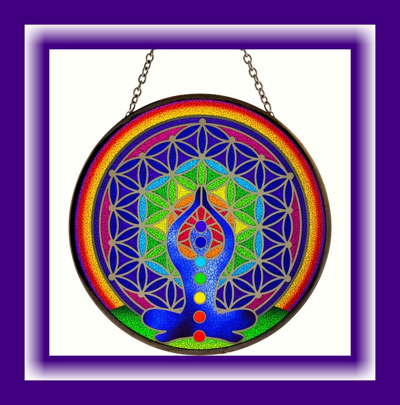 Op de afbeelding: Een kleurrijk glas-in-loodraam dat hangt met een regenboogmandala-ontwerp en een figuur in een yogapose met zeven chakra's.