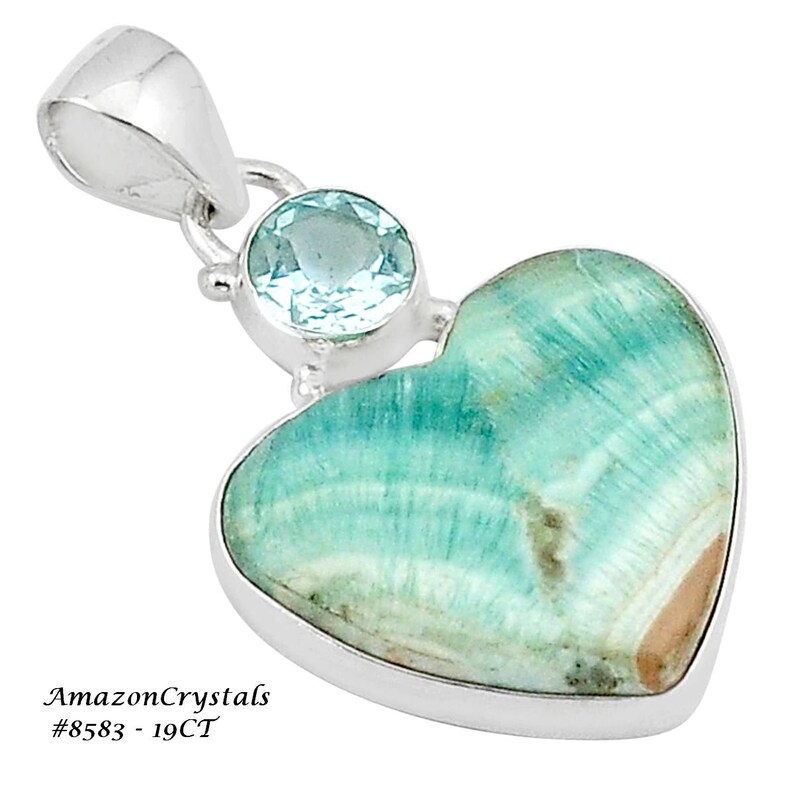 May include: A silver heart-shaped pendant featuring a light blue gemstone and a larger green gemstone. The pendant is set in sterling silver and has a bail for attaching to a chain. AmazonCrystals #8583 - 19CT