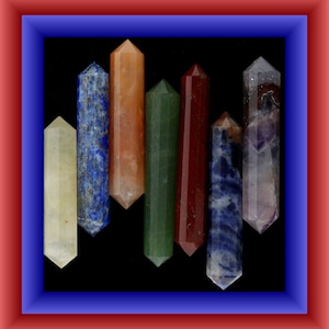 May include: Seven crystal wands in various colours, including clear, blue, orange, green, red, and purple. The wands are arranged in a row, with the tips pointing upwards.