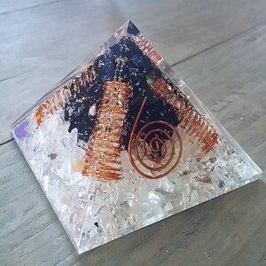 May include: A clear crystal pyramid with a black stone and copper wire spirals inside. The pyramid is filled with small white crystals.