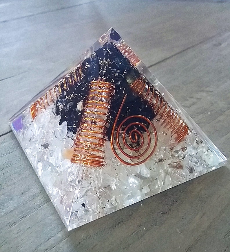 May include: A clear crystal pyramid with a black stone and copper wire spirals inside. The pyramid is filled with small white crystals.