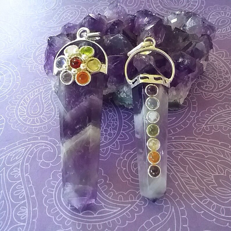May include: Two amethyst crystal pendants with silver settings. One pendant features a circle of colorful gemstones, while the other has a row of smaller gemstones.