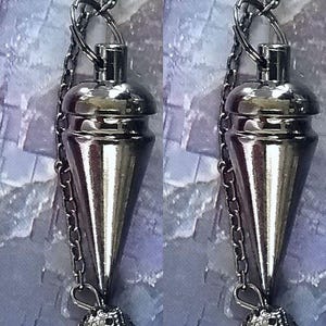 May include: A pair of silver-toned pendulums, each suspended from a chain. The pendulums have a conical shape with a rounded top and a decorative, textured sphere at the bottom. The background has a soft, blurred effect.