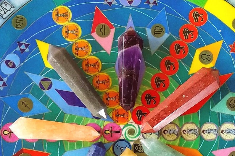 May include: Five polished crystal points in purple, gray, red, orange, and light green are arranged on a circular board featuring colorful geometric patterns, zodiac symbols, and Egyptian iconography including the Eye of Horus and ankh.