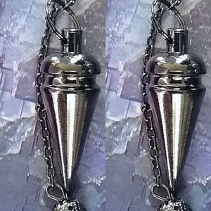 May include: Two silver-toned pendulums hanging from chains. Each pendulum has a conical body and a decorative, textured sphere at the bottom. The chains and pendulums have a shiny, metallic finish, reflecting the light.